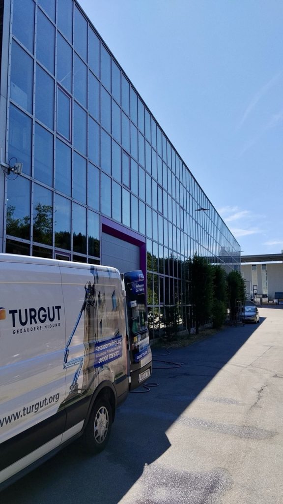 Gereinigte Glasfassade einer Gewerbehalle mit Firmenwagen der Turgut Gebäudereinigung